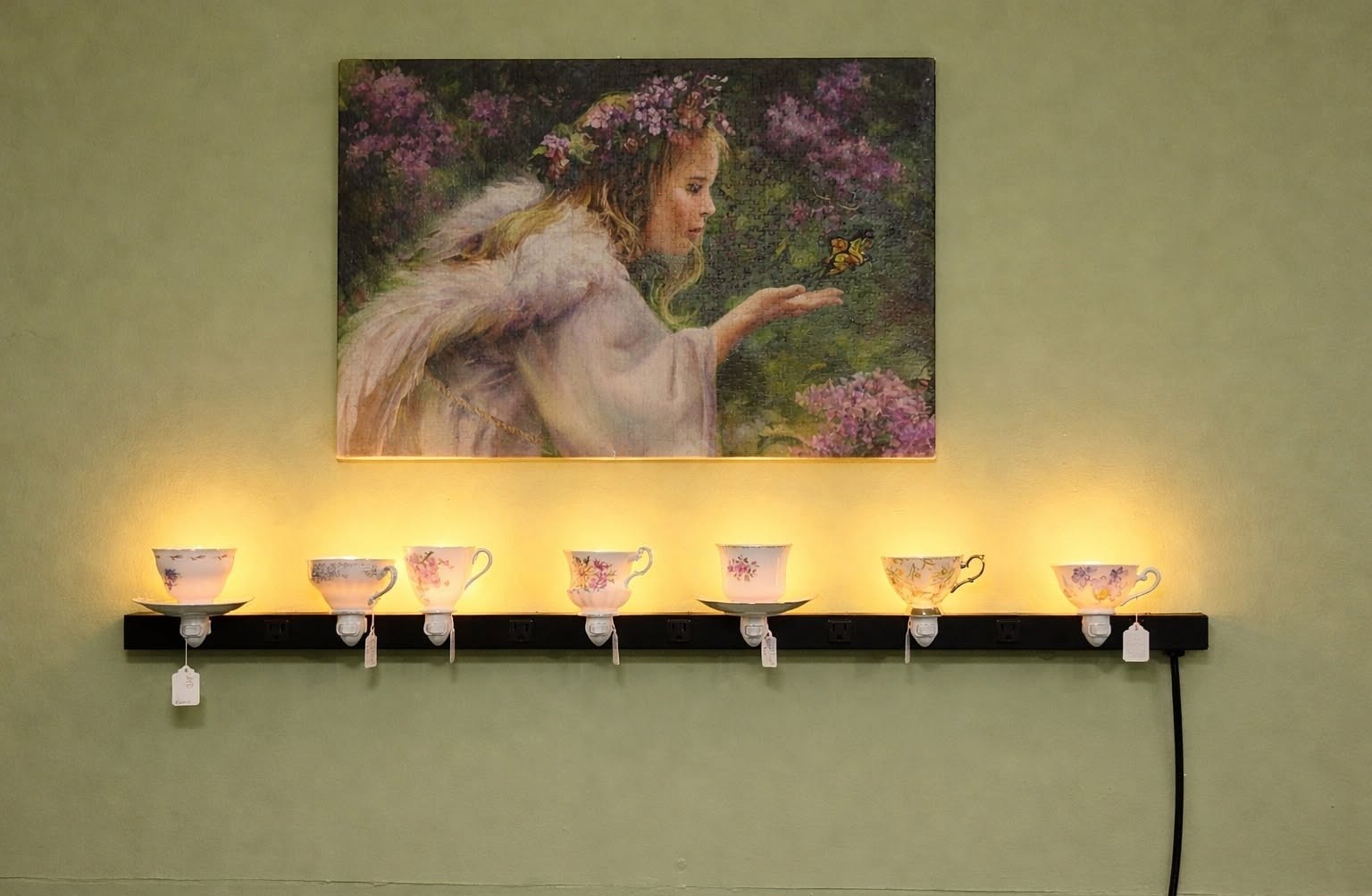 Glowing vintage teacup nightlights by Karen Kidney displayed on a shelf beneath a floral canvas